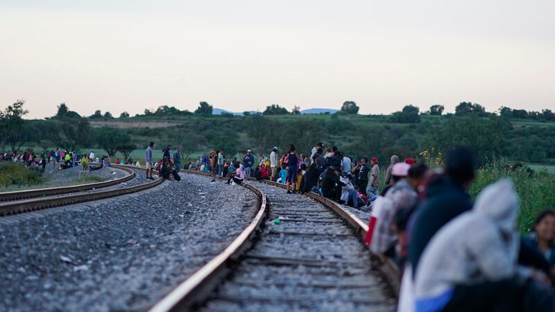 Migrantes esperan a lo largo de las vías con la esperanza de subir a un tren de carga con...